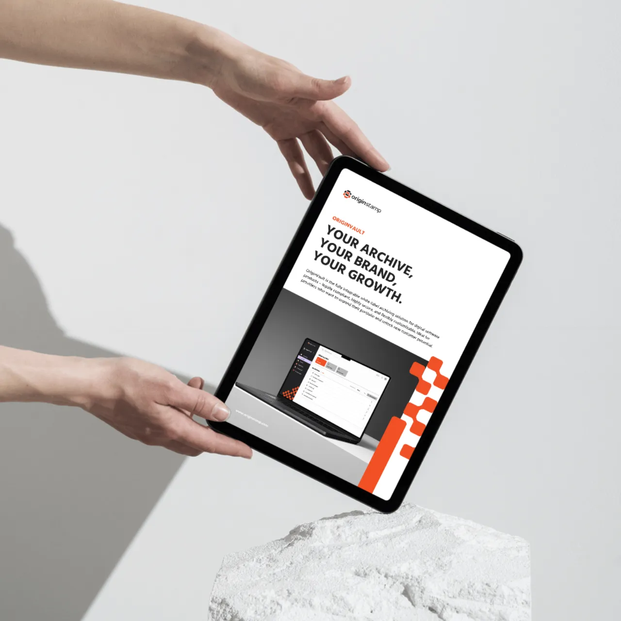 Hands holding a tablet displaying an OriginStamp presentation over a rock.