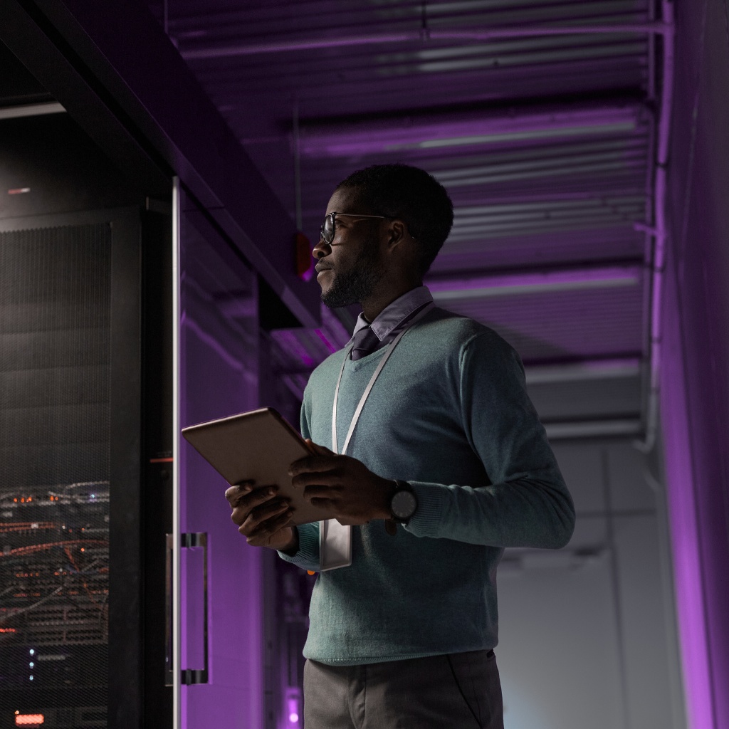 A man stands in his own server room holding a tablet for system monitoring.