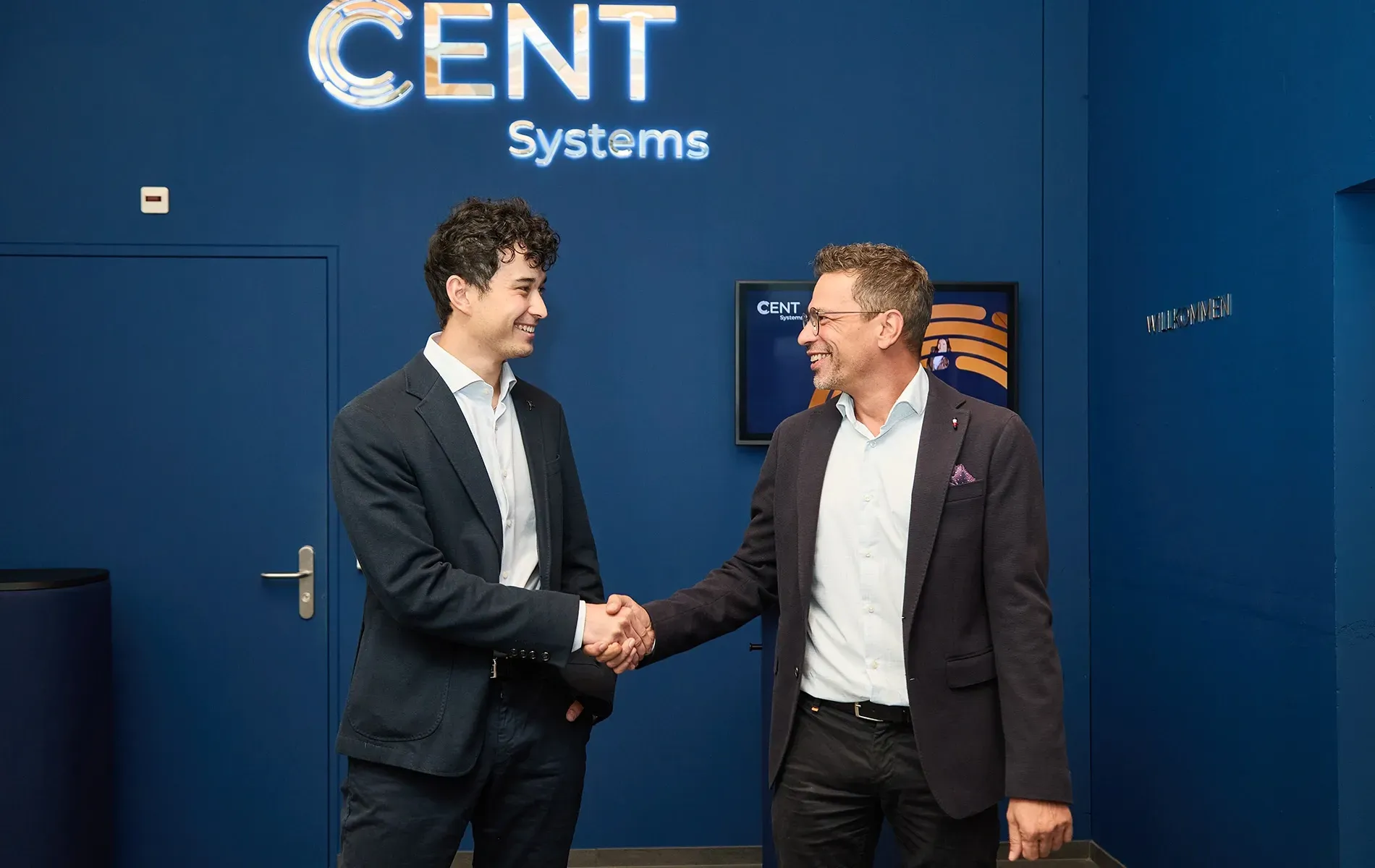Two smiling men shaking hands below a CENT Systems sign.