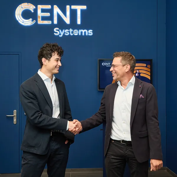 Two men in business attire shake hands before a CENT Systems logo.