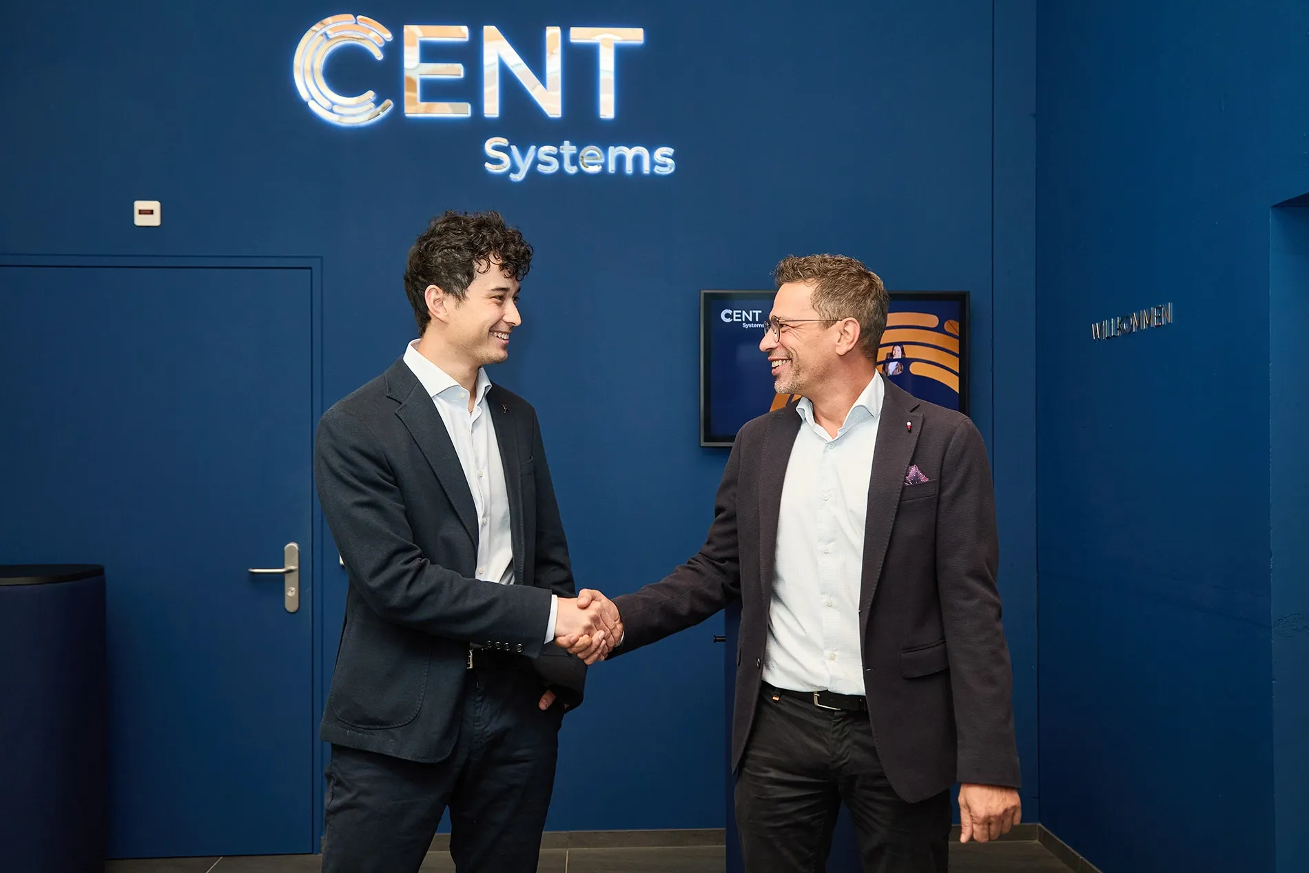 Two men in business attire shake hands before a CENT Systems logo.