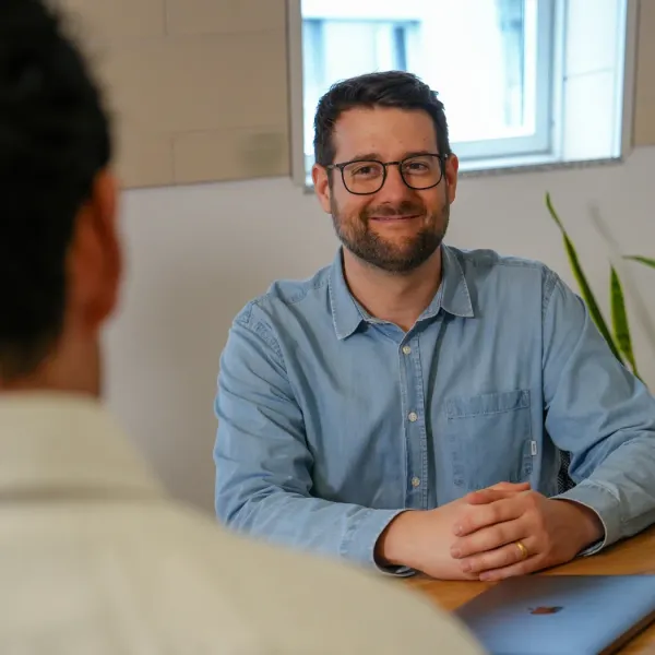 An employee sits at a desk and smiles at a colleague during a meeting.