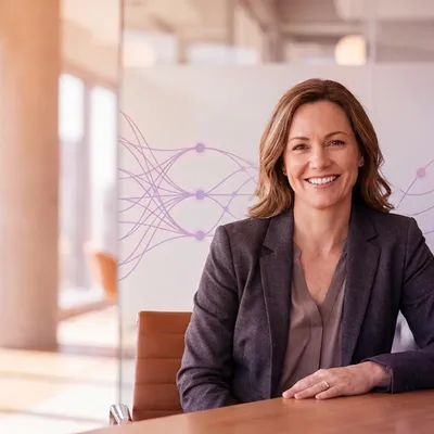 Smiling businesswoman at an office table with abstract digital network graphics in the background.