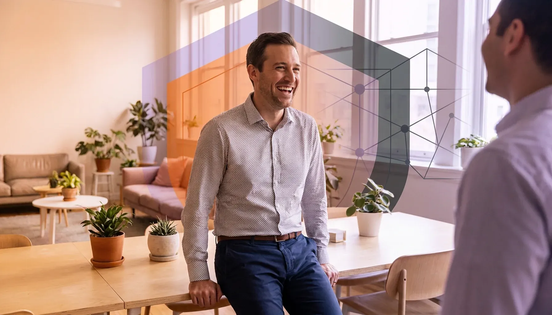 Smiling man leaning on a desk talking to a colleague, with geometric network overlay.