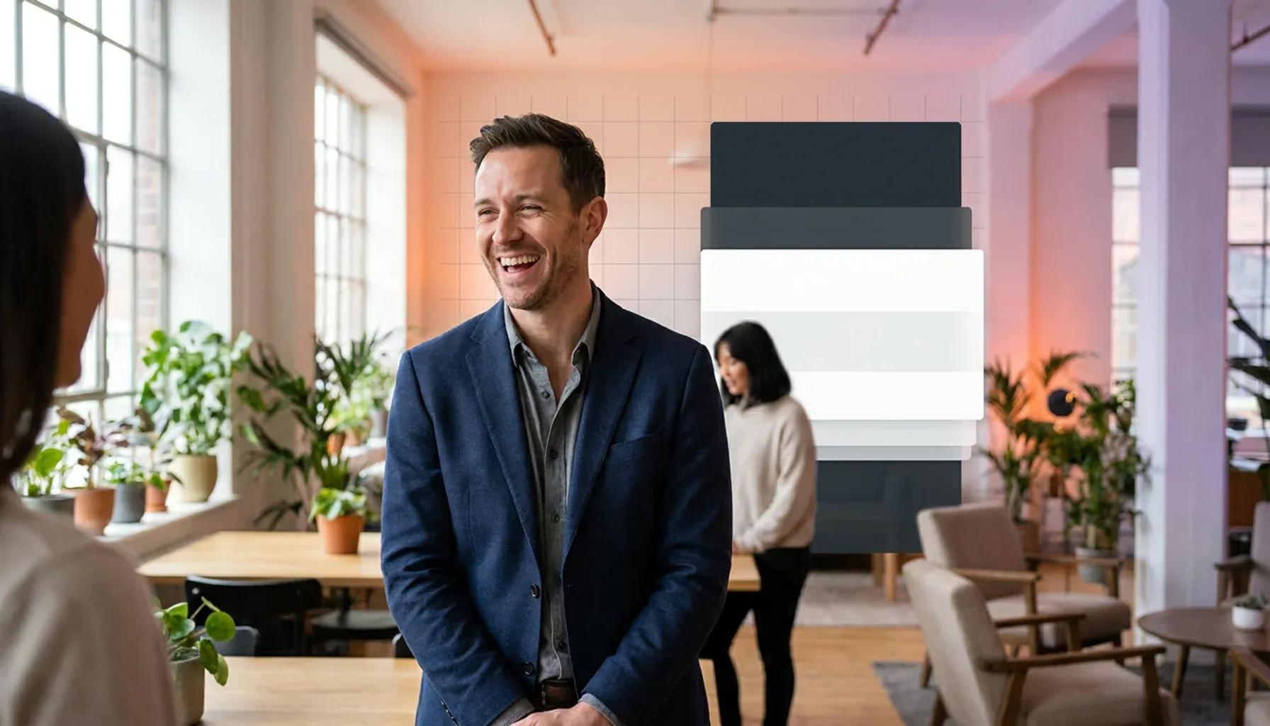 Smiling man in a blue blazer talking to a colleague in a modern office.