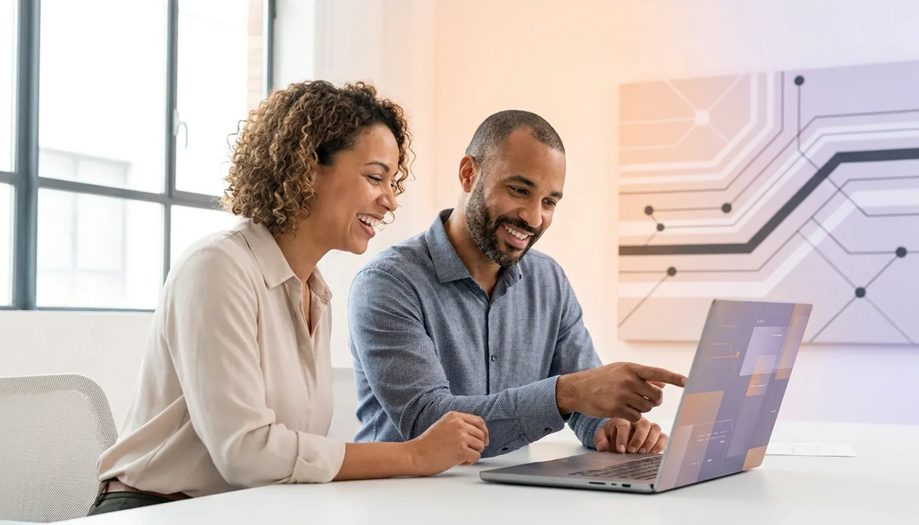 Two smiling colleagues collaborating, with the man pointing at a laptop screen.