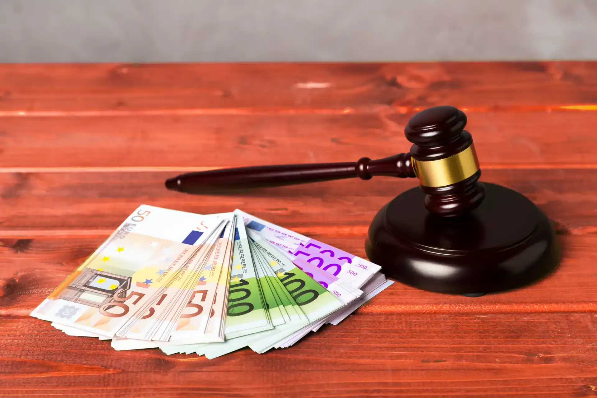 Judge’s gavel next to a stack of euro banknotes on a wooden table, symbolizing legal fines or financial penalties.