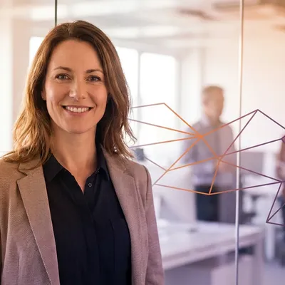 Smiling businesswoman in a modern office with colleagues in the blurred background.