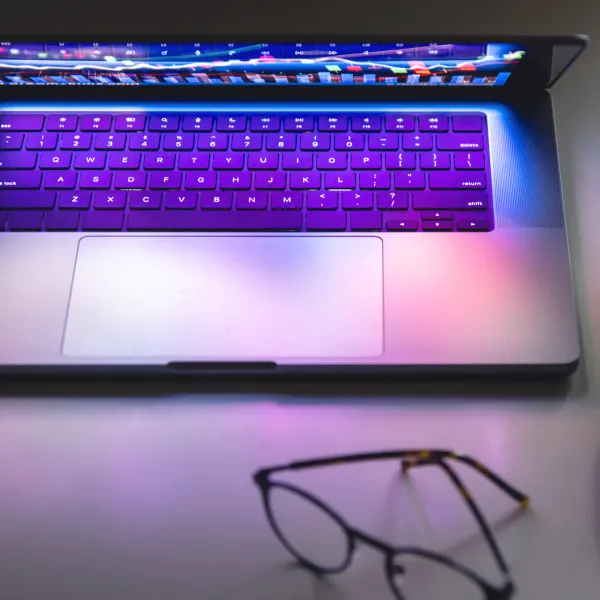 Laptop with illuminated keyboard and glasses in the foreground.