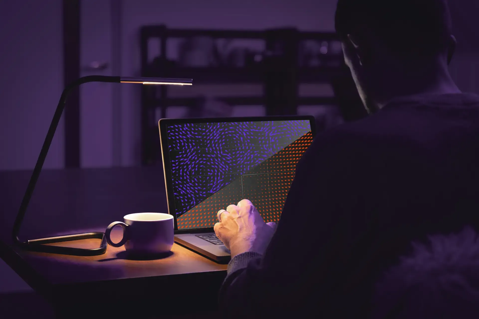Eine Person arbeitet nachts unter einer Lampe an einem Laptop.