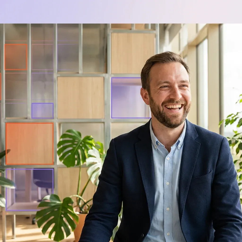 Smiling businessman talking with a colleague in a modern, plant-filled office.
