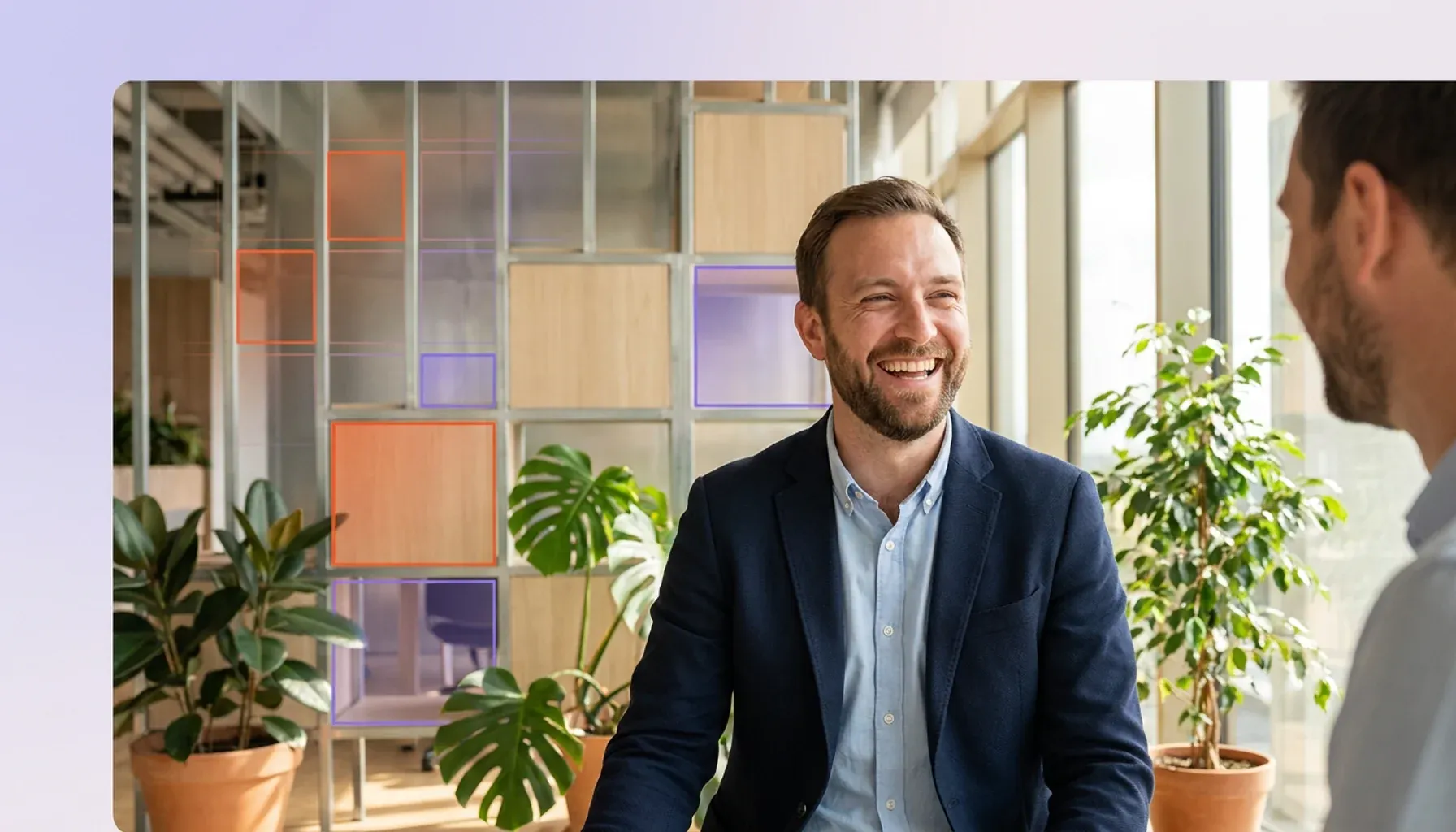 Smiling businessman talking with a colleague in a modern, plant-filled office.