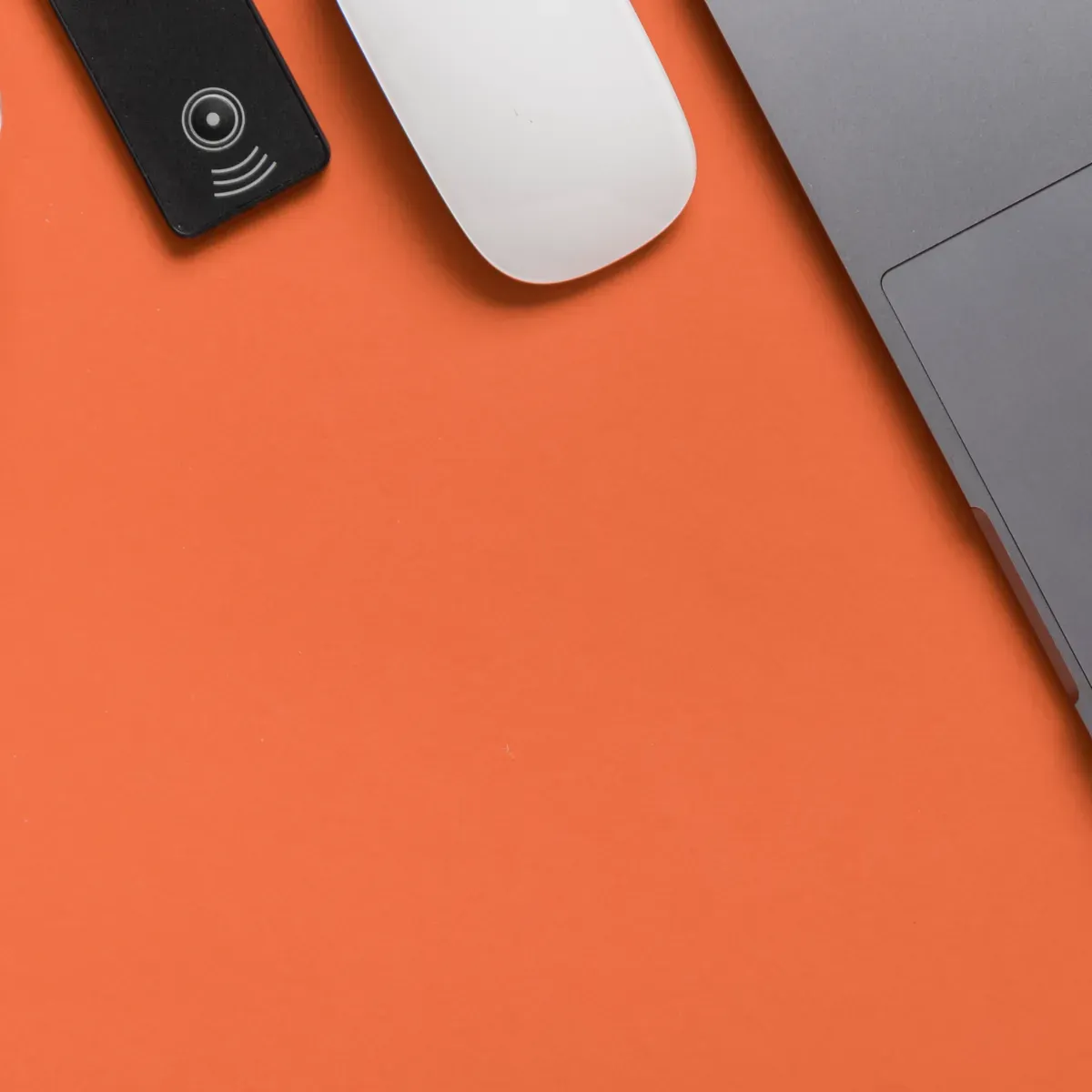 Laptop, mouse and small device on an orange background.