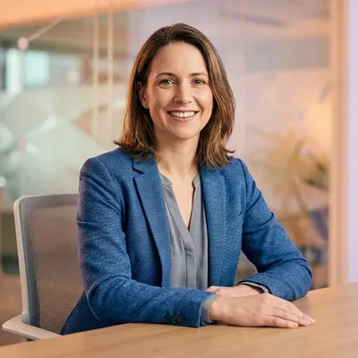 Smiling businesswoman in a blue blazer sitting at a desk in a modern office.