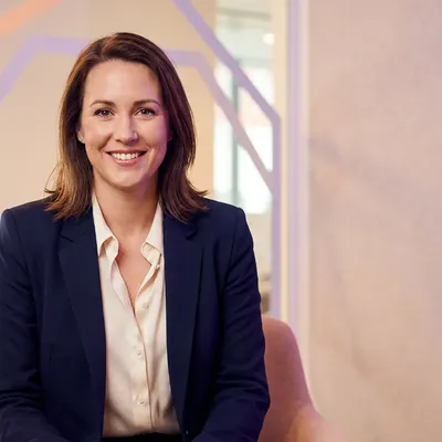 Smiling businesswoman in a navy blazer sitting in a modern office setting.