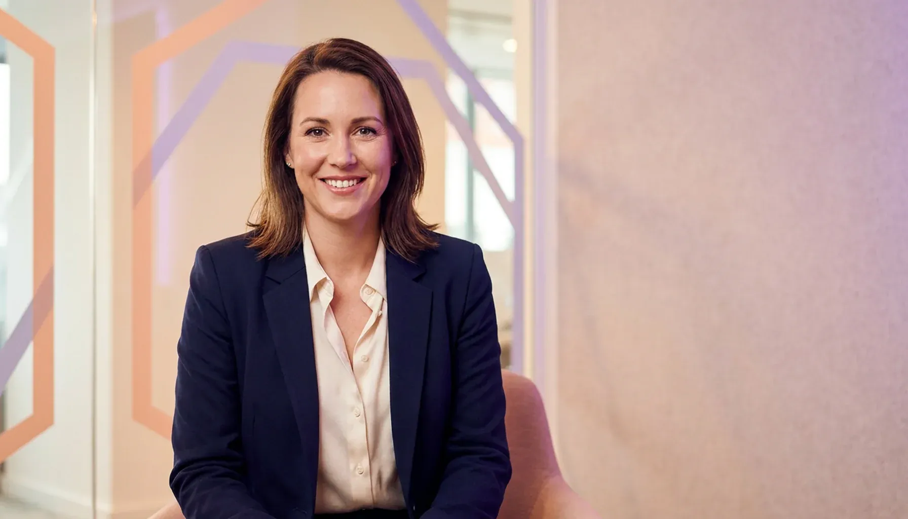 Smiling businesswoman in a navy blazer sitting in a modern office setting.