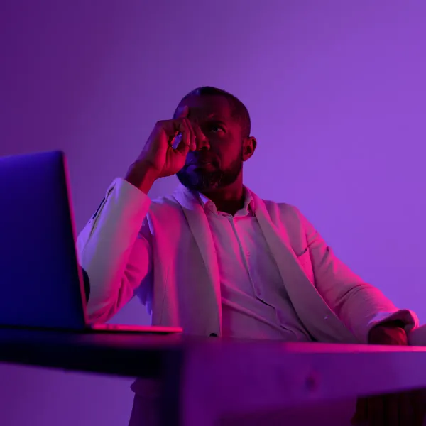 Man sitting thoughtfully in front of a laptop in purple light