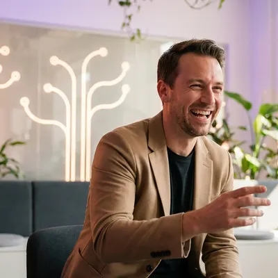 Laughing man in a beige blazer talking with a woman in a modern office.