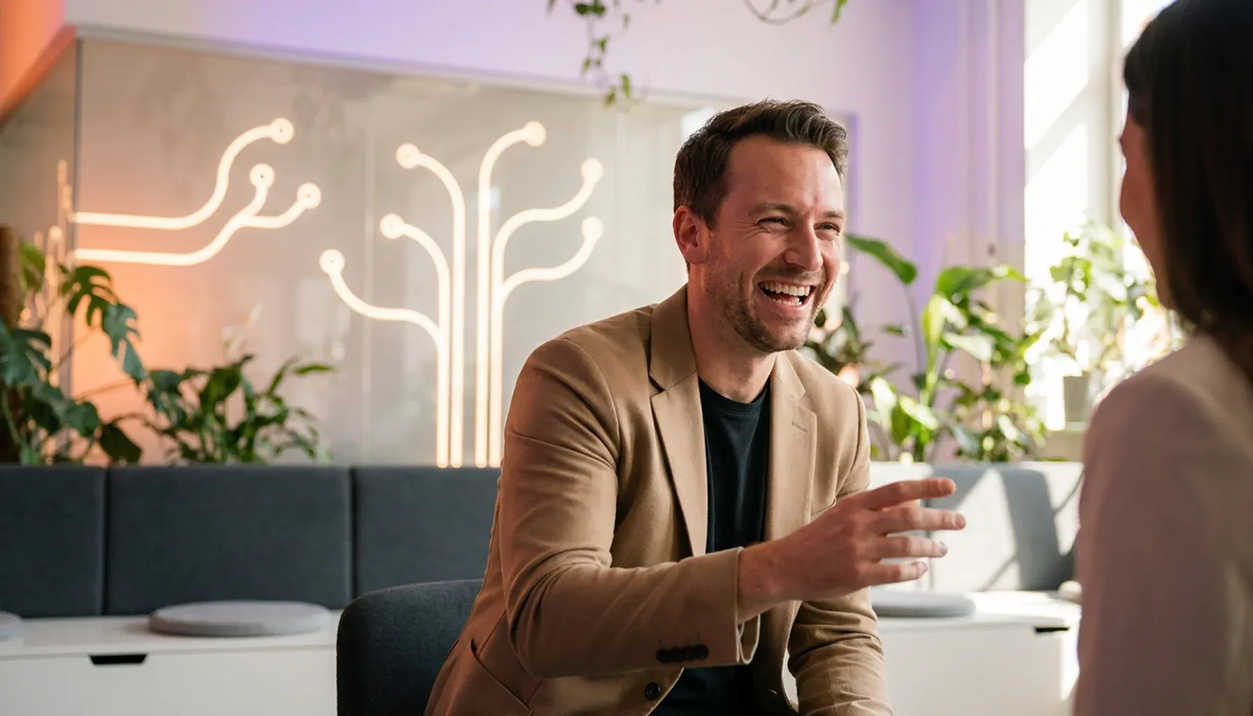 Laughing man in a beige blazer talking with a woman in a modern office.